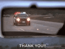 a police car is driving down a highway in a rear view mirror and the words thank you are visible .
