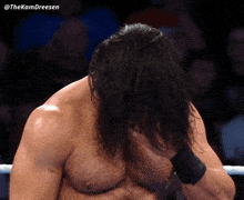 a wrestler with long hair covering his face with his hands