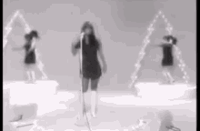 a woman is singing into a microphone in a black and white photo while two women are dancing in the background .