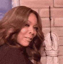 a woman is standing in front of a brick wall and holding a rope .