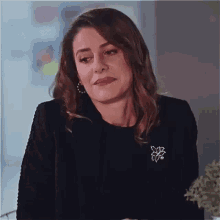 a woman wearing a black jacket and a brooch is sitting in a chair .