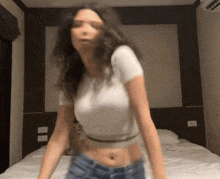 a woman in a white crop top and blue shorts is dancing on a bed