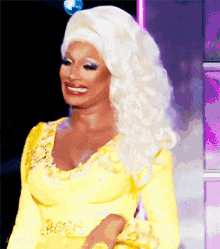 a drag queen wearing a yellow dress and white hair is smiling