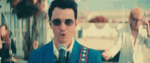 a man in a blue suit is singing into a microphone while wearing sunglasses .