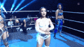 a woman in a white outfit is standing in a wrestling ring with two other women