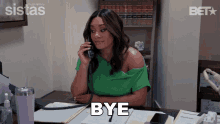 a woman in a green shirt is sitting at a desk talking on a phone and the word bye is above her