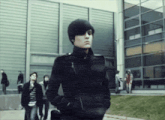 a man in a black jacket with his hands in his pockets stands in front of a building