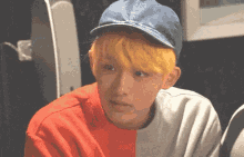 a young man with yellow hair is wearing a blue baseball cap and a red and white shirt .