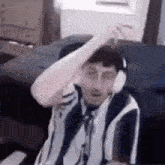 a man wearing headphones and a striped shirt is sitting in a chair in a room .