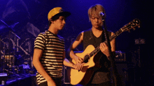 a man in a striped shirt is standing next to a man playing an acoustic guitar