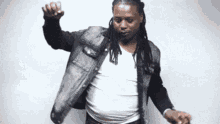 a man with dreadlocks is wearing a denim jacket and a white shirt .