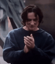 a young man in a blue sweater is clapping his hands together .
