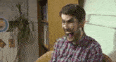 a man in a plaid shirt is making a funny face while sitting in a chair .