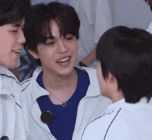 a boy in a blue shirt is smiling and talking to another boy in a white jacket