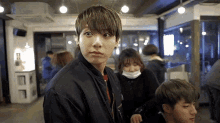 a young man in a black jacket is looking at the camera while standing in a crowded room .