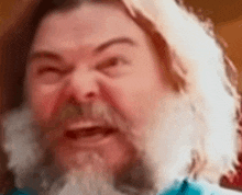 a close up of a man 's face with a beard and long hair making a funny face .