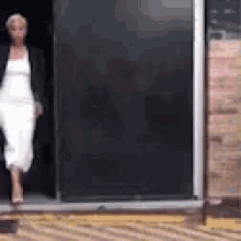 a woman in a white dress is walking out of a door .