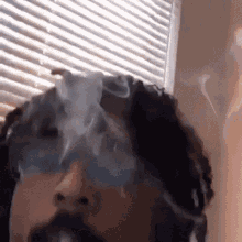 a person with dreadlocks is smoking a cigarette in front of a window .