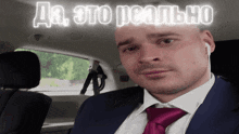 a man in a suit and tie is sitting in the back seat of a car with a sign above him that says да это реально