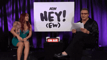 a man and a woman are sitting in front of a sign that says hey ( ew )