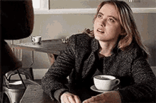a woman is sitting at a table with a cup of coffee and a saucer .