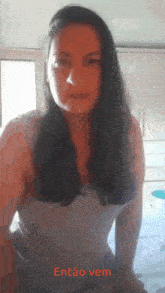 a woman in a white tank top is standing in front of a window with the words então vem written on the bottom
