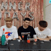 a group of young men are sitting at a table with balloons that say winner days behind them