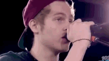 a young man is singing into a microphone while wearing a hat and bracelet .
