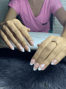 a woman in a pink shirt has a ring on her finger and her nails are painted white