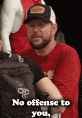 a man wearing a red shirt and a black hat says no offense to you