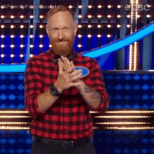 a man with a beard wearing a plaid shirt is clapping his hands on a stage .