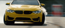 a yellow bmw is driving down a road with smoke coming out of the tires