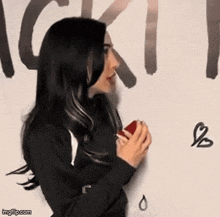 a woman in a black sweater is holding a red object in front of a wall that says " ick "