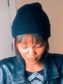 a woman wearing a black beanie and a black leather jacket has her eyes closed