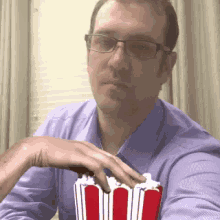 a man wearing glasses holds a bucket of popcorn in his hand
