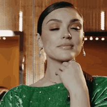 a woman wearing a green dress and earrings is looking down with her hand on her chin .
