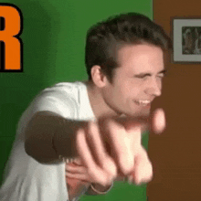 a man in a white shirt is pointing at the camera with his hands .