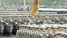 a large group of soldiers marching in a line with a flag in the background