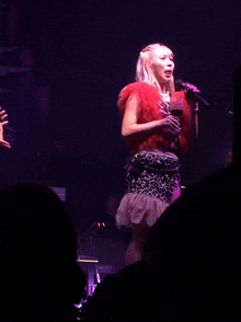 a woman in a leopard print skirt sings into a microphone in front of a mesa keyboard
