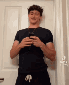 a young man in a black shirt is standing in front of a white door holding a cell phone .
