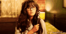 a woman with glasses is holding a curling iron in her hand while sitting on a bed .
