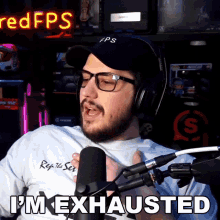a man wearing headphones and glasses says i 'm exhausted in front of a microphone