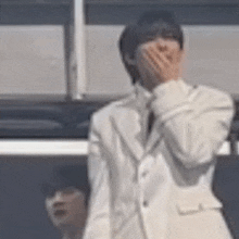 a man in a white suit and tie is covering his mouth with his hand .