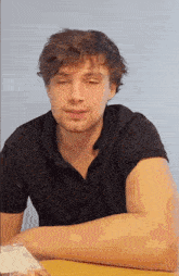 a man in a black shirt is sitting at a table with his eyes closed and his arm crossed .
