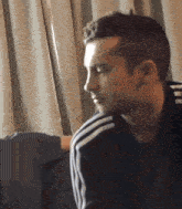 a man in an adidas jacket is sitting on a couch in front of a window