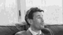 a man in a suit and tie is sitting on a couch making a funny face .