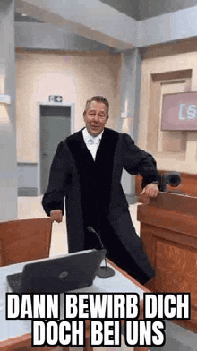 a man in a judge 's robe is standing in front of a laptop computer in a courtroom .