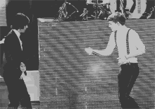 a black and white photo of two men dancing in front of a wall that says direction