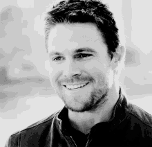a black and white photo of a smiling man in a leather jacket