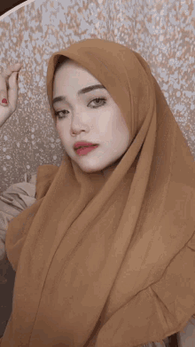 a woman wearing a brown hijab is smiling and looking at the camera